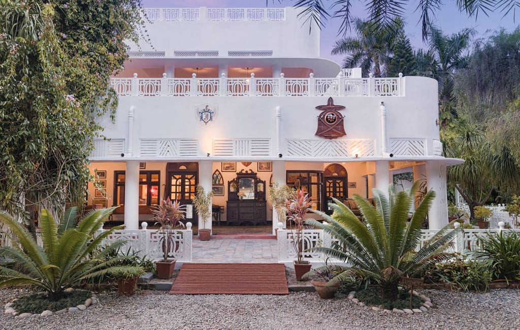 White art deco manor facade framed by palms and ferns at dusk at Jaagir Manor, Dudhwa