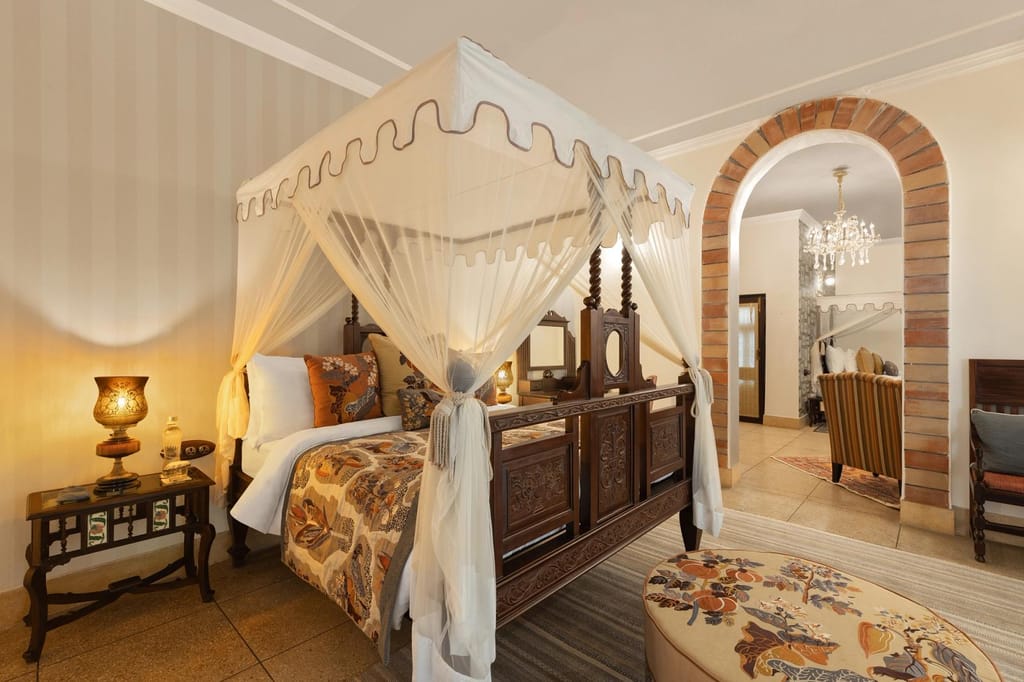 Premium Suite With King Bed with carved four-poster bed under a canopy and brick archway to the sitting room at Jaagir Manor, Dudhwa