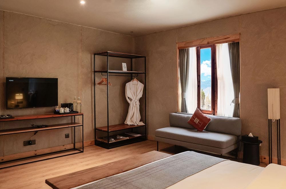 Club Room seating corner with grey daybed sofa, open hanging rail with bathrobes and wall-mounted TV at The Chospa, Leh