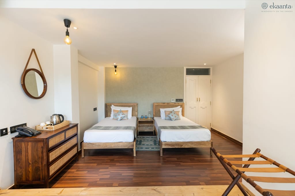 Ganga View Room with two cane-headboard beds, wooden floor and rattan chest of drawers at Ekaanta, Haridwar