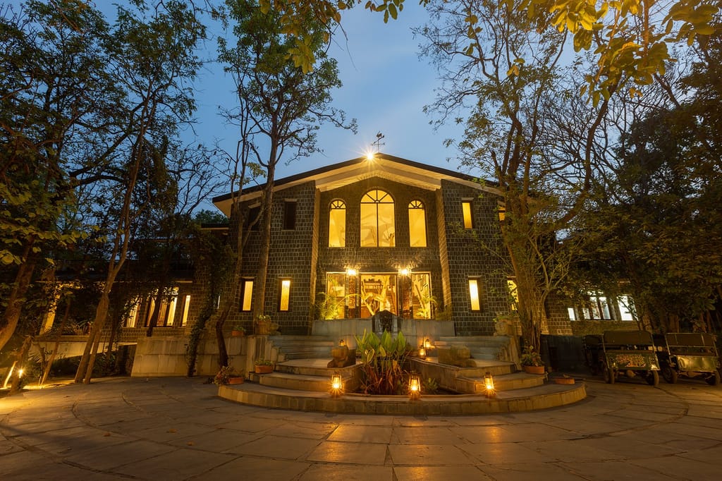 Stone main lodge lit with lanterns at dusk, safari jeeps parked to the side at Singinawa Jungle Lodge, Kanha