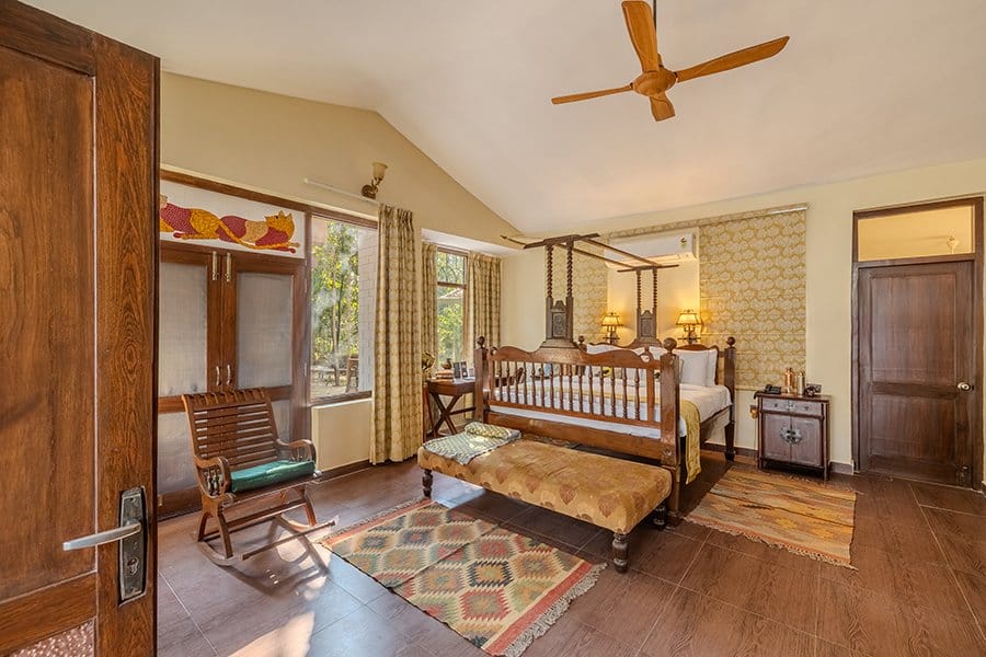 The Perch — bedroom with carved wooden four-poster bed, rocking chair and garden-facing windows at Singinawa Jungle Lodge, Kanha