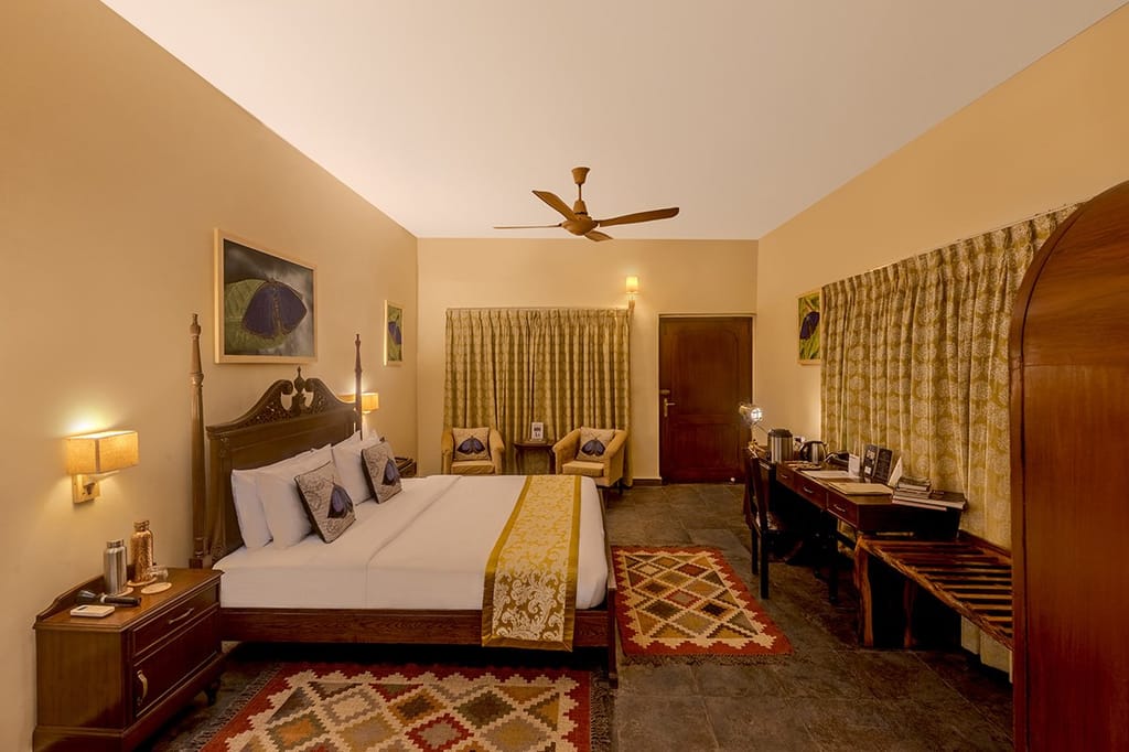 The Wildernest — four-poster bed with gold runner, kilim rugs and writing desk at Singinawa Jungle Lodge, Kanha