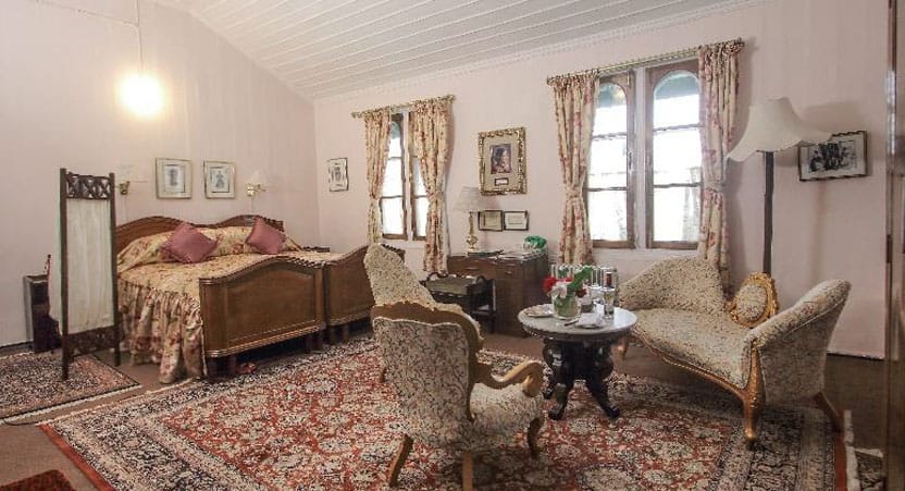 Princess of Siam room at Windamere Hotel with a wooden double bed, chaise longue and armchairs around a marble-top table on a large carpet