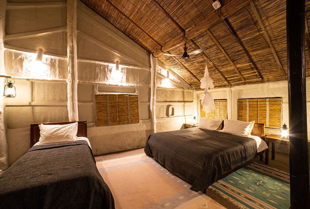 Traditional Room with a double bed and a single bed under a woven reed ceiling at Tiger Tops Tharu Lodge, Chitwan