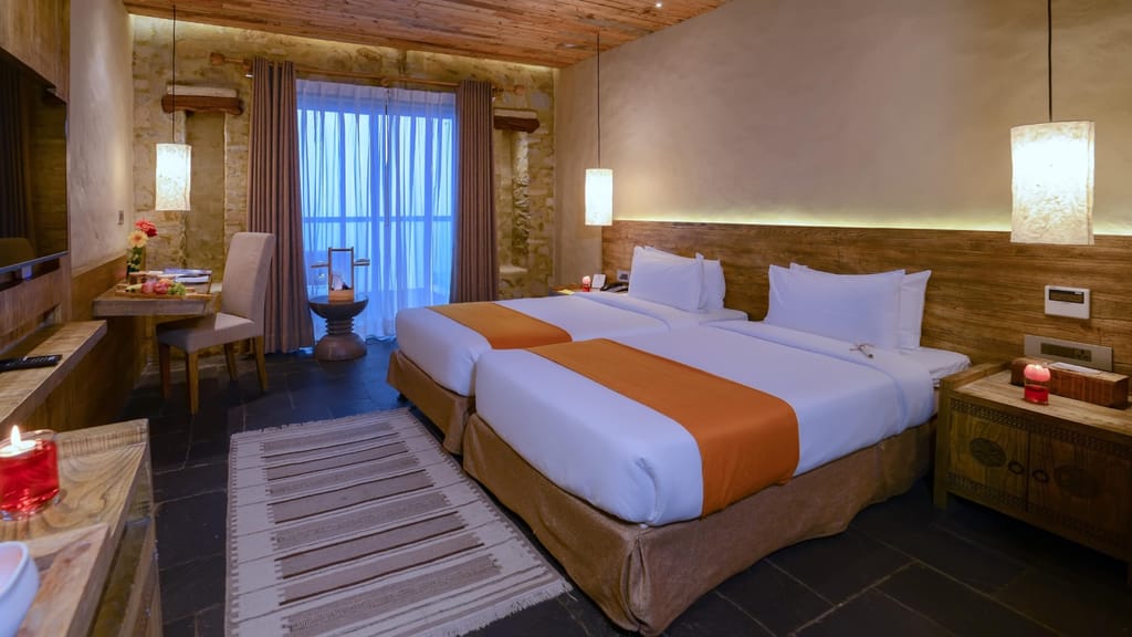 Deluxe Rooms twin beds with orange runners, stone walls and a timber ceiling at Sarangkot Mountain Lodge, Pokhara