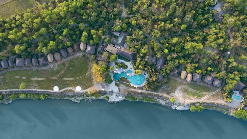 Aerial view of thatched lodge buildings and a freeform pool beside the river at Barahi Jungle Lodge, Chitwan