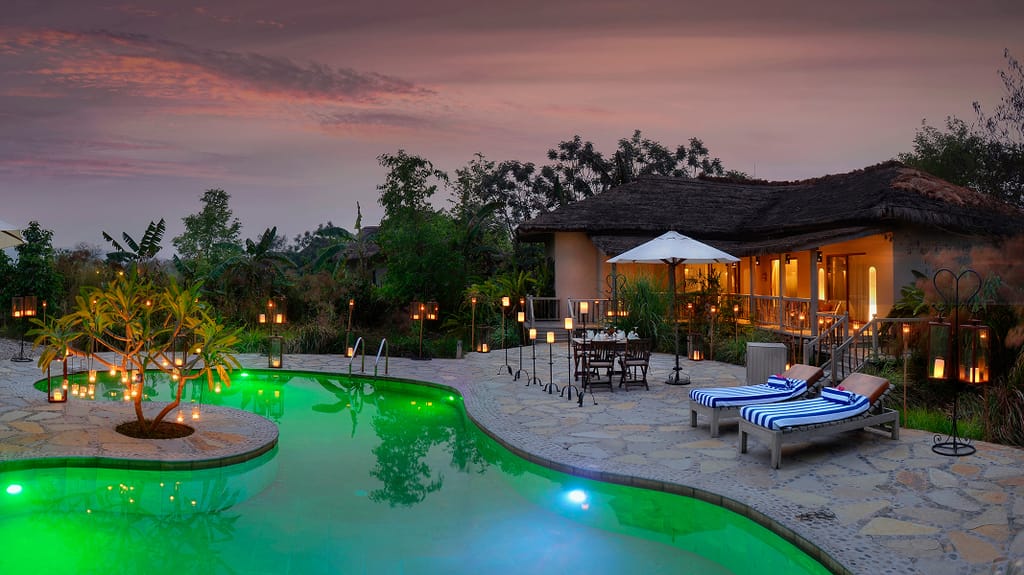 Presidential Suite thatched villa and lantern-lit pool terrace at dusk at Barahi Jungle Lodge, Chitwan
