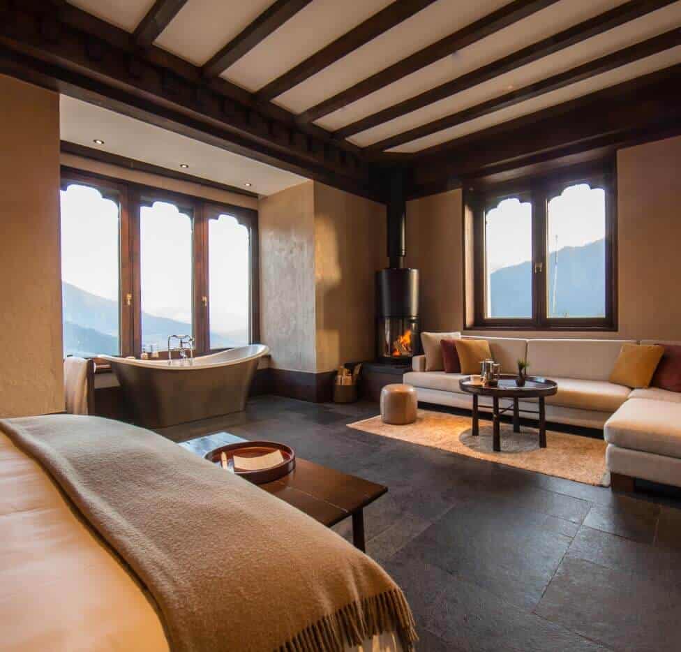 Bhutanese Farmhouse Suite with a bed, freestanding bathtub by the window, wood-burning stove and sofa at Gangtey Lodge, Gangtey
