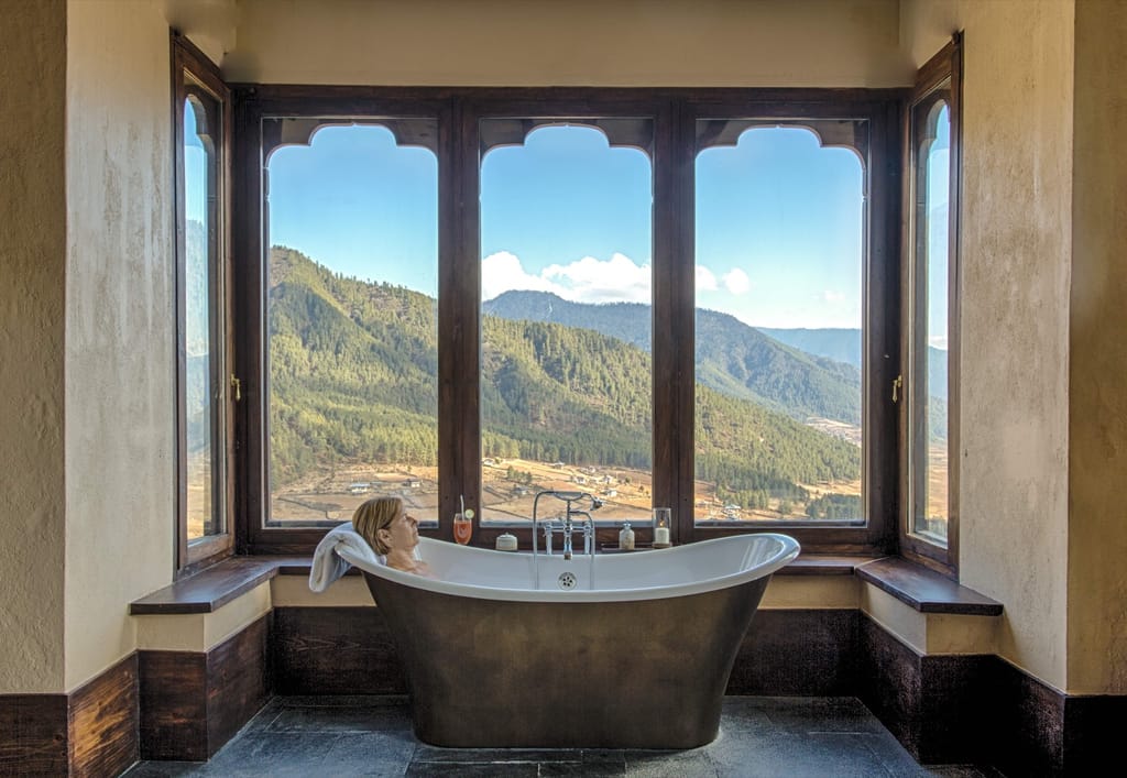 Bhutanese Farmhouse Suite guest relaxing in a bathtub with valley views through arched windows at Gangtey Lodge, Gangtey