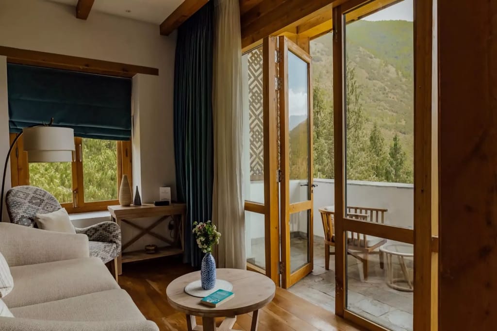 Balcony Room sitting area with a sofa, armchair and folding doors opening to a private balcony with mountain views at Bhutan Spirit Sanctuary, Paro