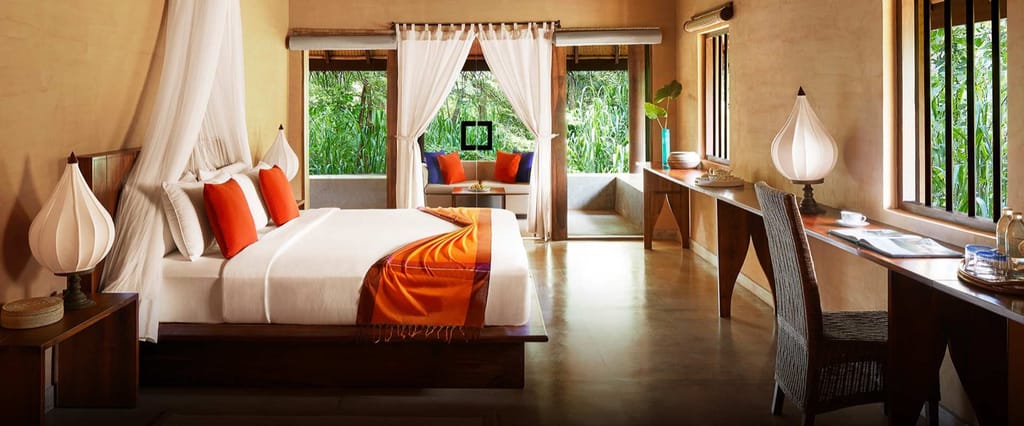 Garden Dwelling bedroom with canopied bed, orange cushions and doors opening to a private sitting terrace at Jetwing Vil Uyana, Sigiriya