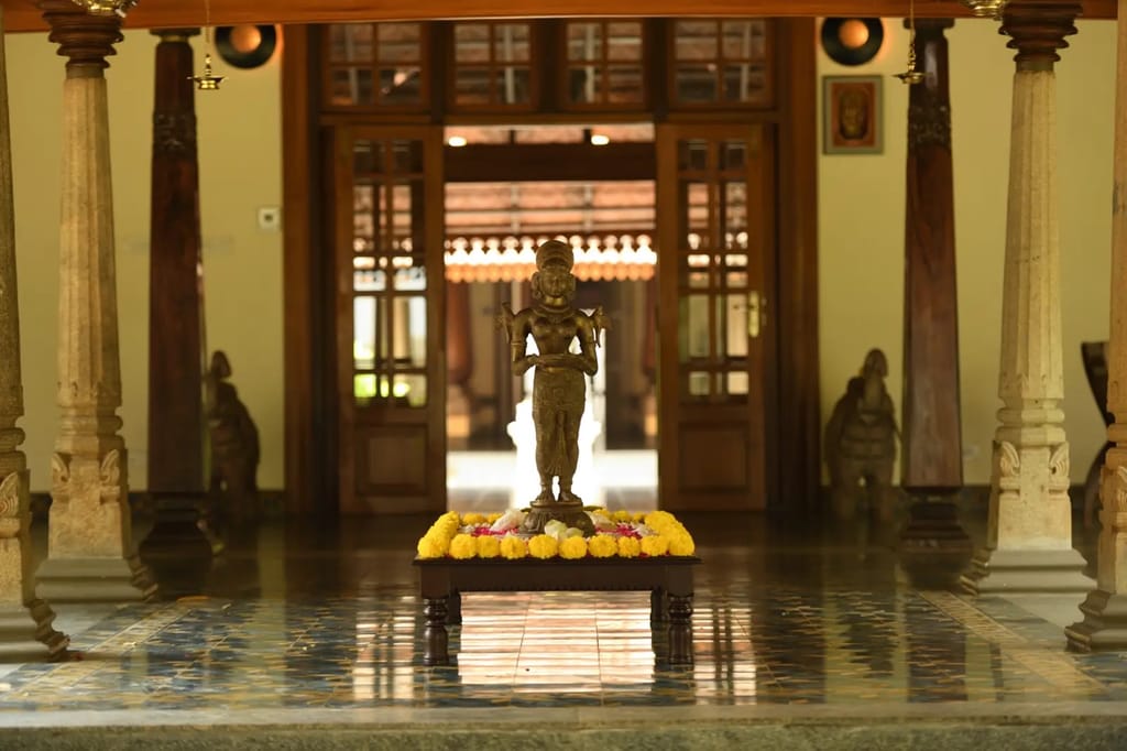 Bronze deity statue ringed with marigold flowers in a stone-pillared hall at Svatma, Thanjavur
