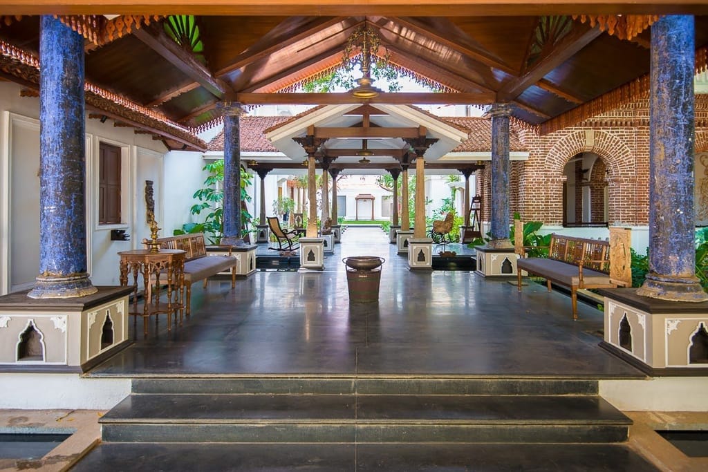 Pillared courtyard pavilion with blue stone columns, wooden benches and polished dark floor at Svatma, Thanjavur