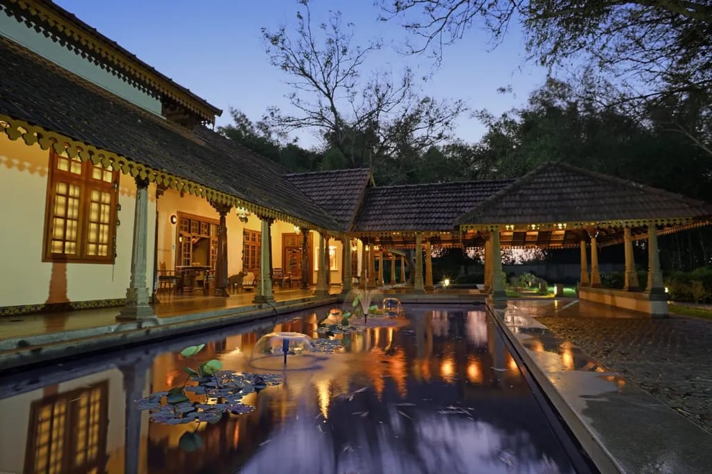 Courtyard water feature with fountains beside lamplit tiled-roof verandahs at dusk at Svatma, Thanjavur