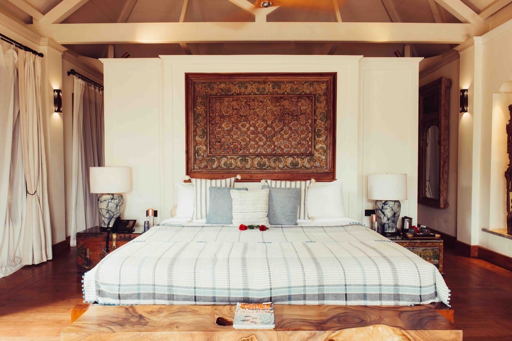 Bedroom with a large carved wooden panel above the bed and beamed ceiling at Kahani Paradise, Gokarna