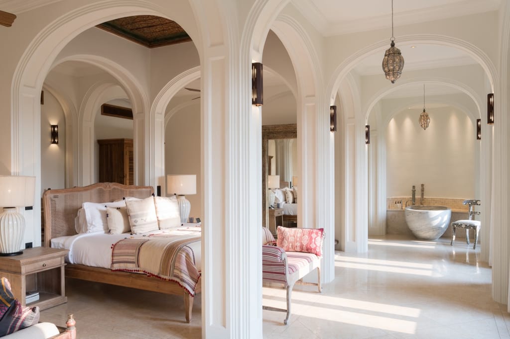 Queen Suite bedroom with the bed set between white arches, hanging lanterns and a marble bathtub beyond at Kahani Paradise, Gokarna