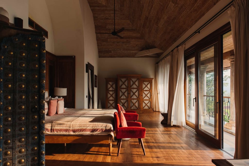 Suite bedroom with vaulted timber ceiling, red velvet armchairs and glass doors to a private balcony at Kahani Paradise, Gokarna