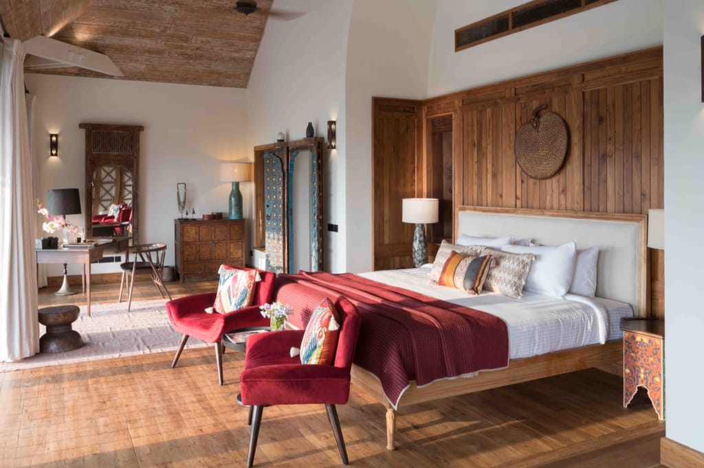 Suite bedroom with teak-panelled bedhead wall, red armchairs and antique painted furniture at Kahani Paradise, Gokarna