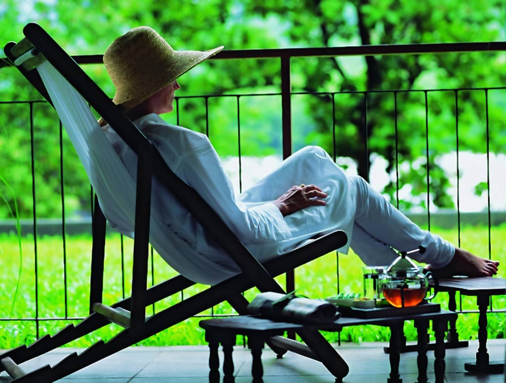 Luxury room balcony with a guest reclining on a sling chair beside a tea tray, Rainforest Athirapally, Athirappilly