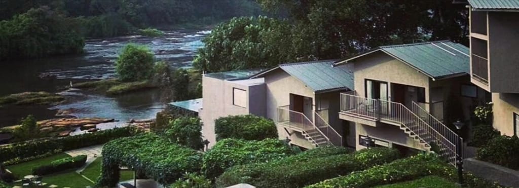 Deluxe Cottage exteriors on a landscaped slope above the rocky river, Niraamaya Retreats Samroha, Athirappilly