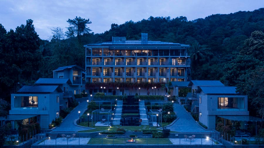Main retreat building and villas lit up at dusk against a forested hillside at Niraamaya Retreats Samroha, Athirappilly