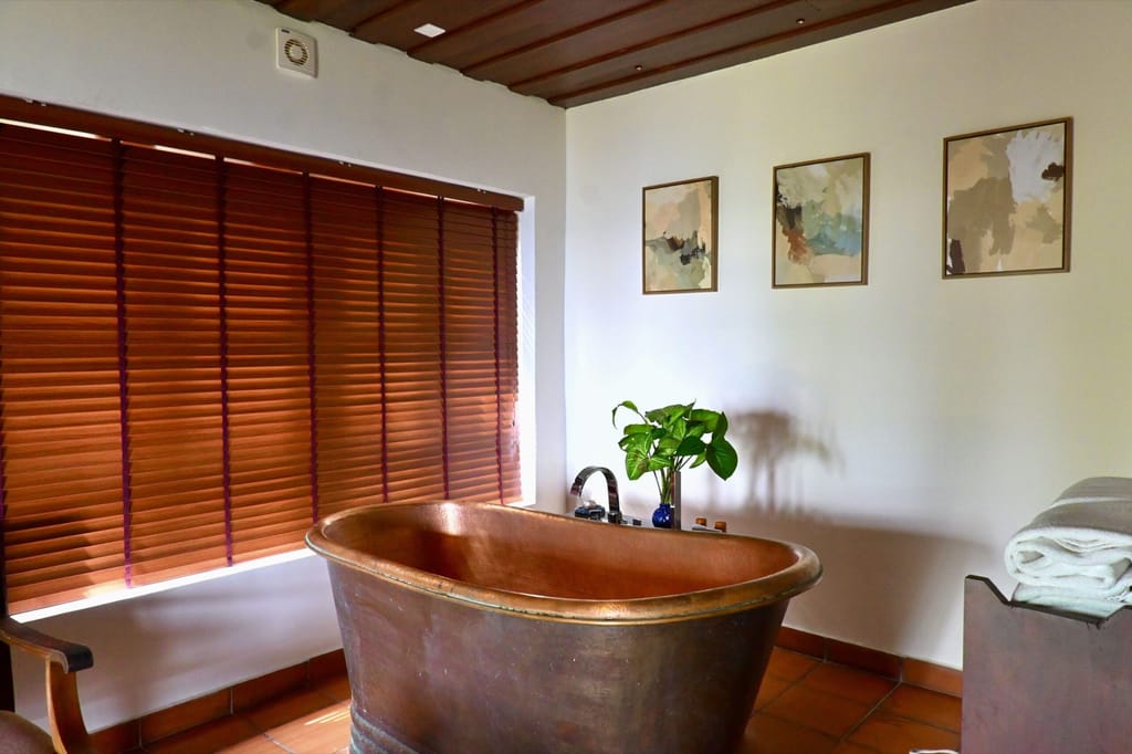 Honeymoon Spa Suite bathroom with freestanding copper tub, wooden blinds and framed art, Spice Tree Munnar, Munnar