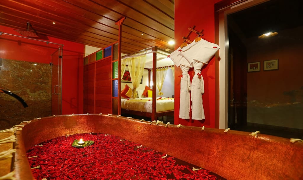 Honeymoon Spa Suite copper bathtub filled with rose petals beside a four-poster bed, Spice Tree Munnar, Munnar