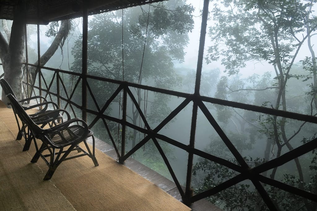 Tree House balcony with cane chairs overlooking mist-covered rainforest, Vythiri Resort, Vythiri