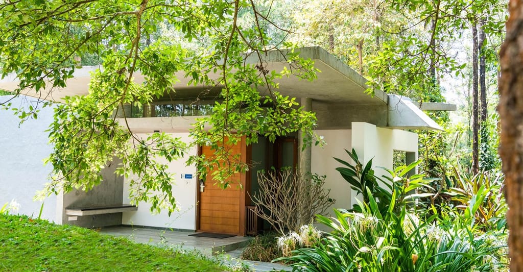 Qahva villa entrance with timber door and flat concrete canopy beneath forest canopy at Java Rain Resort, Chikmagalur