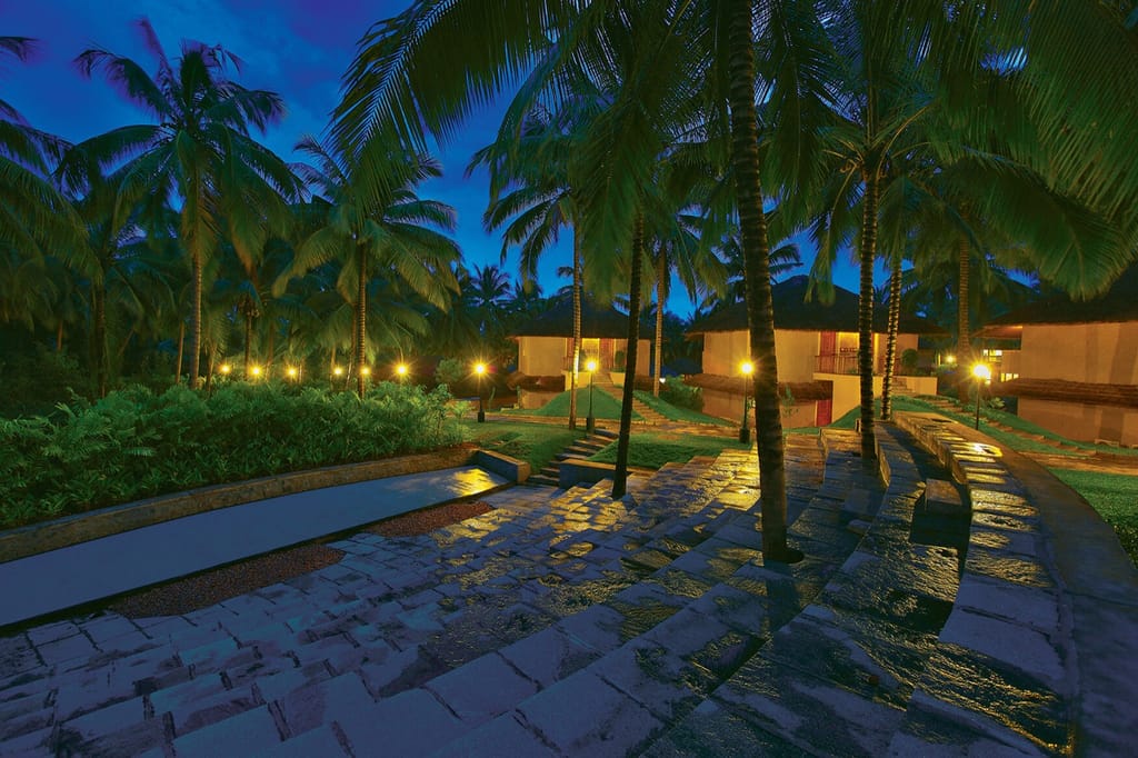 Lamp-lit stone pathways and cottages amid coconut palms at dusk, Coco Lagoon by Great Mount, Pollachi