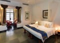 Deluxe Room at The Malabar House: carved wooden bed with mosquito net, stone floor and windows onto the garden