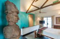Carved stone bust beside the bed under timber beams in The Malabar Suite at The Malabar House