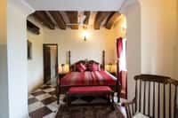 Bedroom with a four poster bed under exposed timber beams and a chequerboard marble floor