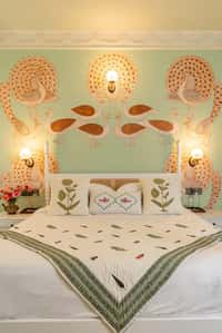 Bed below hand-painted peacocks on a green wall