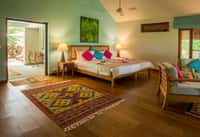 Cottage bedroom with a wooden floor, kilim rugs and doors open to the garden
