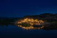 Boulder outcrop lit with lamps beside water at night