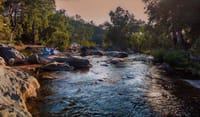 Guests seated on rocks beside the river at a jungle lunch spot, Fort Dhariyawad, Dhariyawad