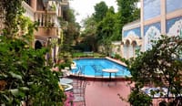 Pool and painted courtyard wall seen through the garden, Jas Vilas, Jaipur