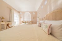 Pink-plastered bedroom with arched cane headboard and Krishna wall relief, Niravi, Jaipur