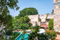 Stone-clad Estate wing and tiled pool seen through frangipani and palms, Niravi, Jaipur