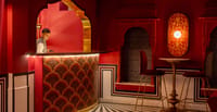 Red-lacquered courtyard bar with gold mosaic counter and carved jharokha niches, Padmaa, Jaipur