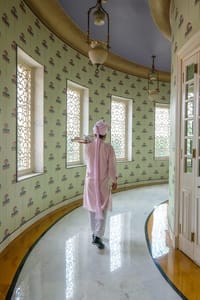 A curved room papered in pale green parasols, tea being carried through