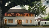Old Harbour Hotel, Fort Cochin: the white two-storey Dutch-style mansion with tiled roof under a large rain tree, upper windows lit at dusk