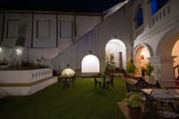 The Old Courtyard Hotel courtyard lawn at night with cast-iron garden tables under the lit arches