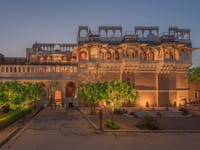 Palace facade lit at dusk, tiers of arched jharokha galleries above the entrance courtyard