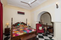 Bedroom with a carved four poster bed, patchwork quilt and green and white marble floor