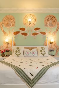 Bed below hand-painted peacocks on a green wall