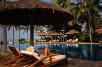 Infinity pool with thatched parasols and loungers, the sea beyond the palms