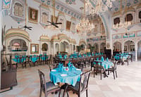 Frescoed dining hall under chandeliers, tables laid with blue linen